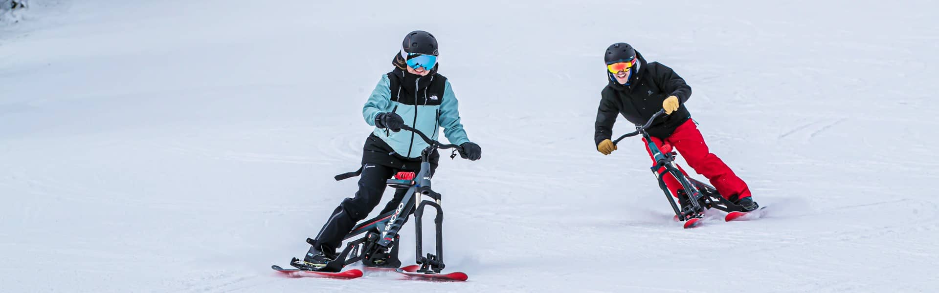 Two people riding Sno-Gos on a groomed run