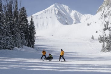 Skiers, one in a sit-ski, skiing with Lone Peak in the background